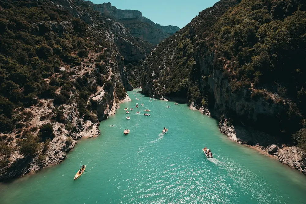 a group of people in boats in a river with Verdon Gorge in the background